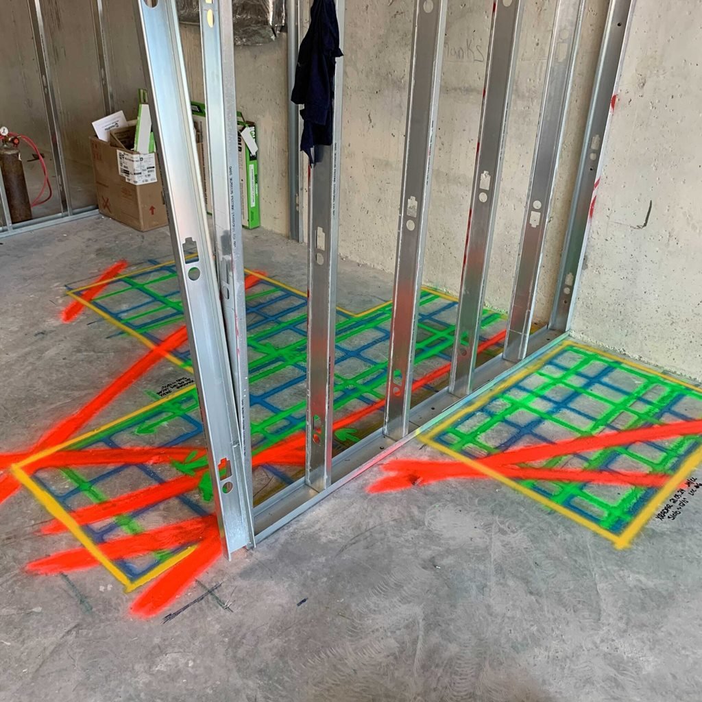 GPR scan areas marked in yellow, green, blue and red on a concrete slab around steel wall studs
