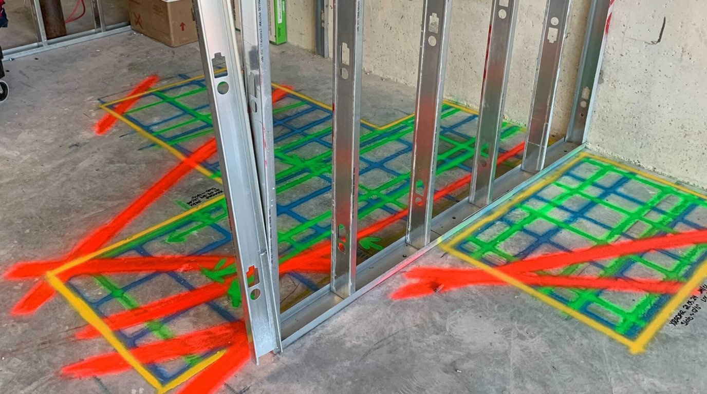 Colour-coded GPR scan markings on a concrete slab beside a steel stud wall